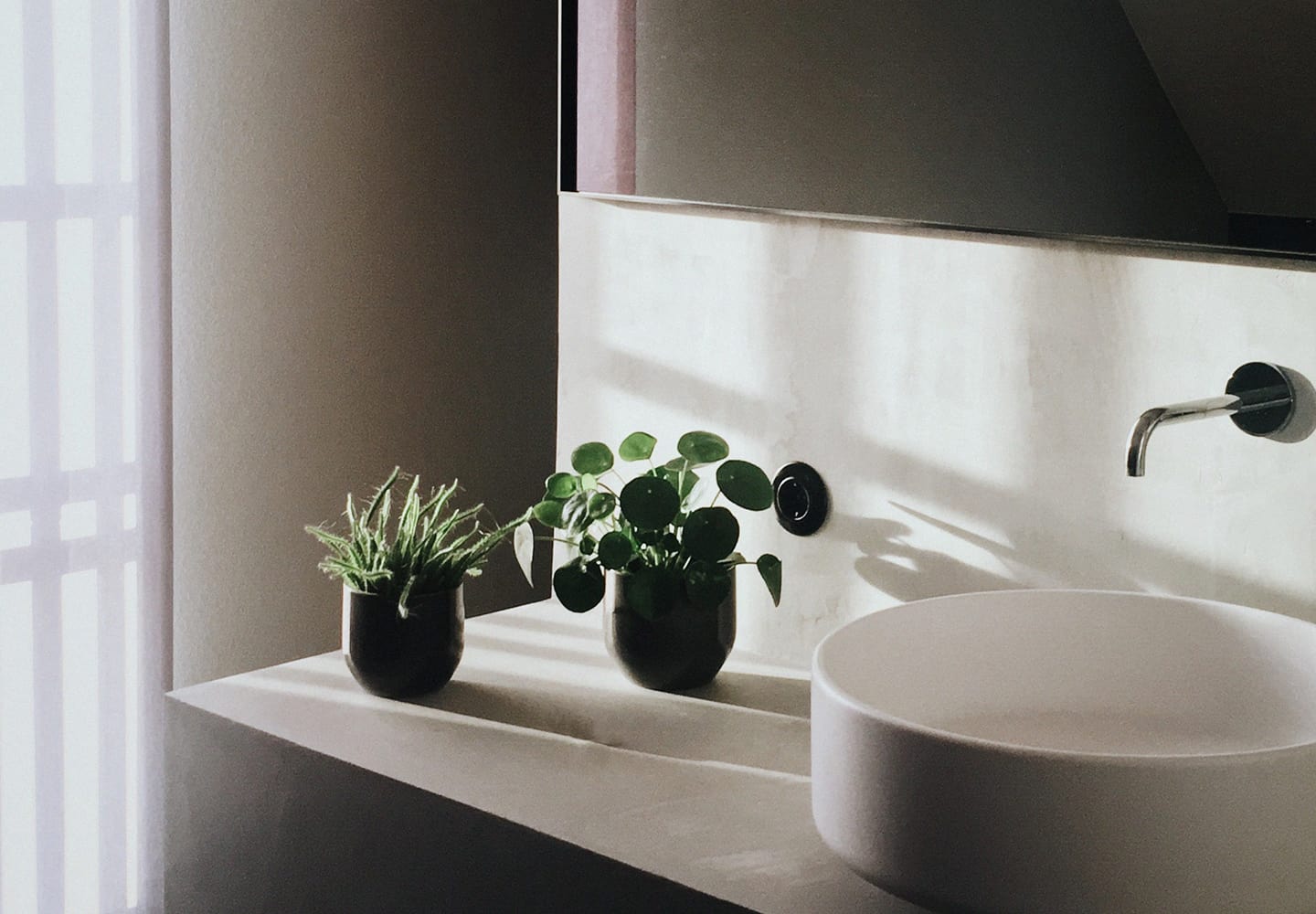 Soft lit bathroom counter and sink featuring small plants